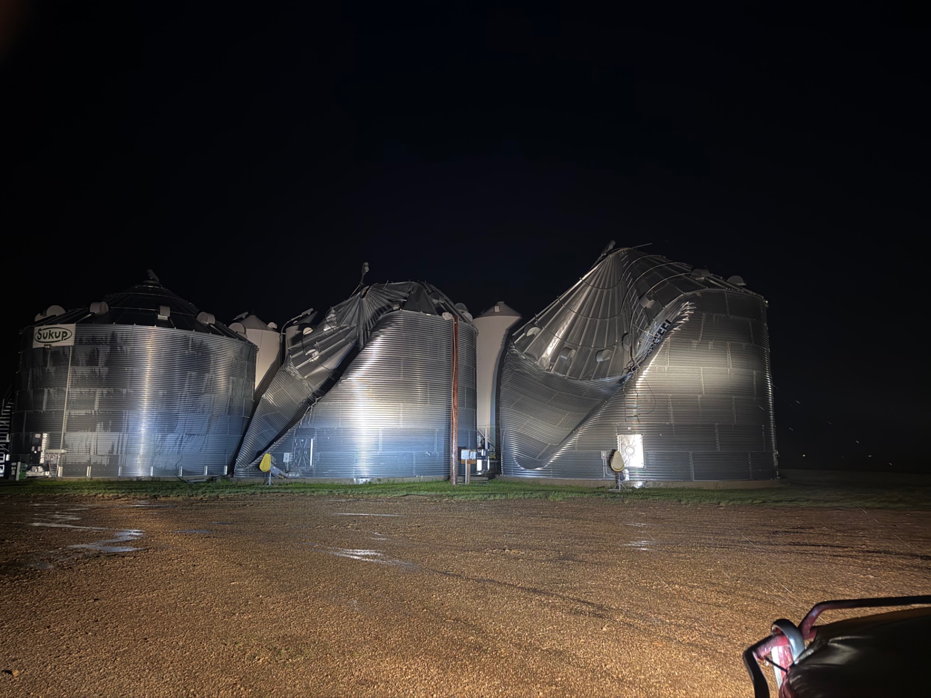 Three grain bins lit at night on Sletten Farms under a wide North Dakota sky